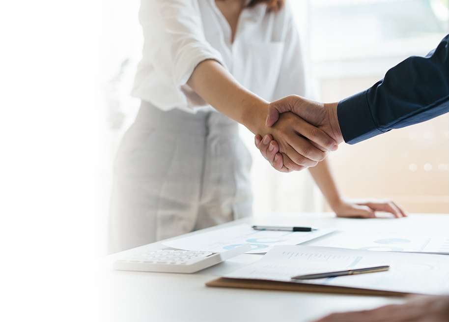 Two business people shaking hands at a desk.